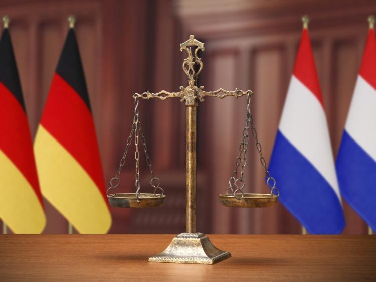 Waga adwokacka na tle flagi niemieckiej i holenderskiej